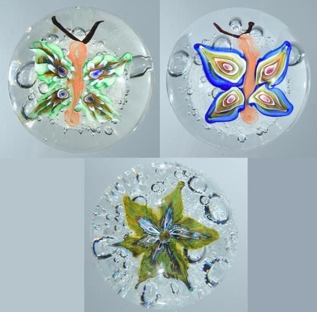 Trois presse-papiers dont deux à motif de papillon polychrome sur fond bullé (réparation à une base), et un presse-papiers à motif de fleur polychrome en trois dimensions sur fond bull