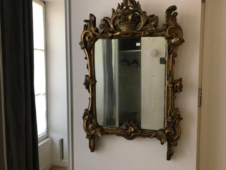 Un miroir en bois doré sommé d'une corbeille fleurie et de pampres de vigne