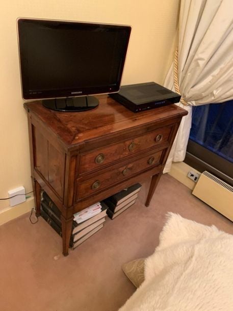 • Une commode en bois naturel présentant deux tiroirs en façade et reposant sur quatre pieds gaine