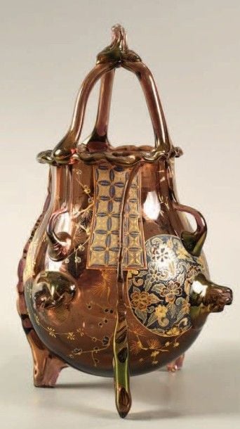 Vase tripode en verre violet; décor de panneaux émaillés ornés de fleurs et de motifs géométriques; bord, anse à trois branches, appliques et pieds travaillés à la pinc