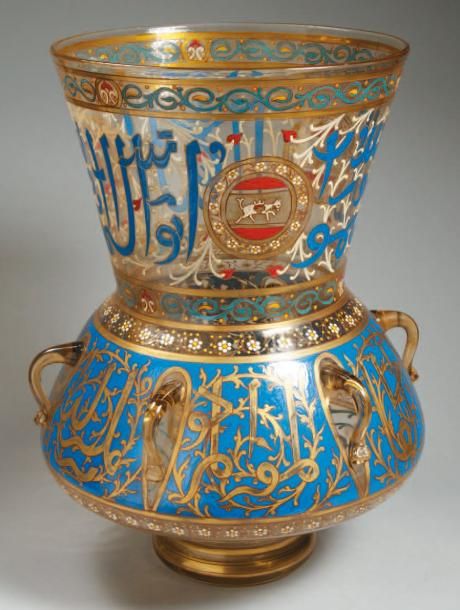 VERRE ÉMAILLÉ Lampe de mosquée de style mamelouk en verre translucide, à panse discoïde, base évasée et col muni de deux anses, décorée en émaux polychromes et or de deux larges bandeaux épigraphiques et de « blasons » ornés d'un cheval, entre des rinceaux de fleurette