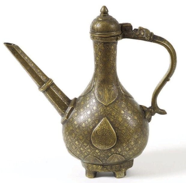 Verseuse indienne Fonte de laiton à décor incrusté de pâte noire Inde, XVIIIe - XIXe siècle Hauteur: 29 cm - La panse de cette aiguière est centrée d'un médaillon fleuri sur un semis de fleurs, typique des décors de l'époque moghole, l'anse à décor zoomorphe évoque le makara, animal marin, véhicule de la déesse du Gange, Gang