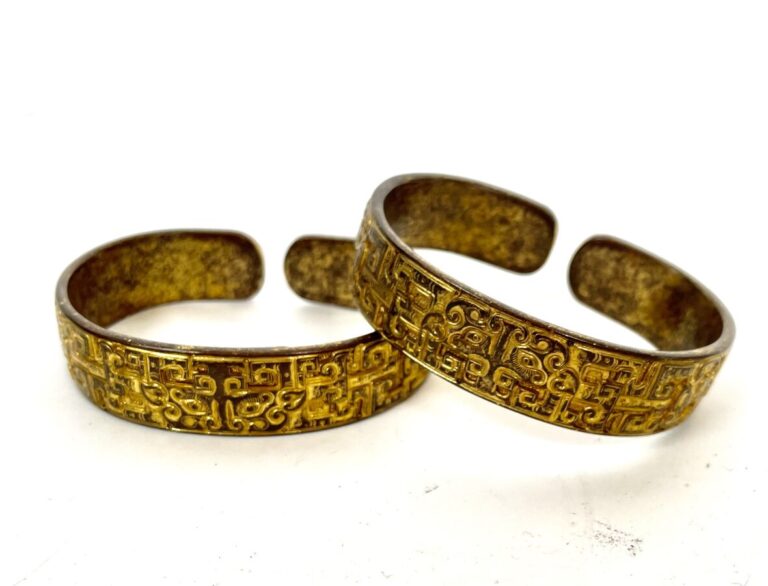 Ensemble de deux bracelets en métal doré, à décor de volutes et masques de Taot…