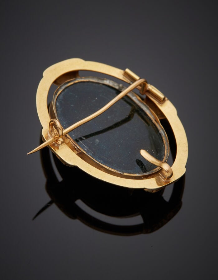 BROCHE ovale en or jaune (750‰) ajouré et ciselé, ornée d'une plaque d'onyx fla…
