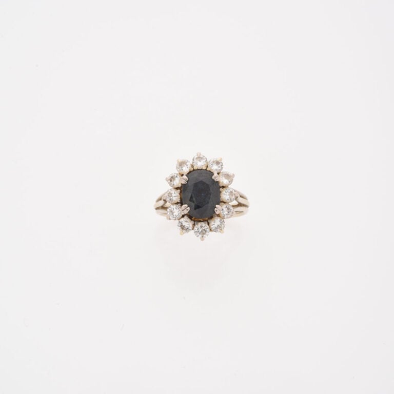 Bague marguerite en or gris (750) ornée d'un saphir de taille ovale facettée da…