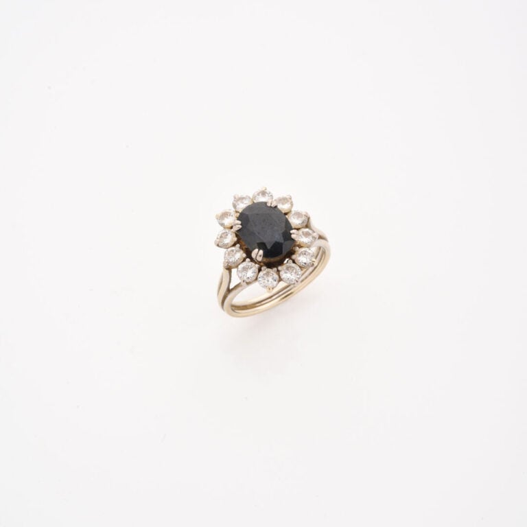 Bague marguerite en or gris (750) ornée d'un saphir de taille ovale facettée da…