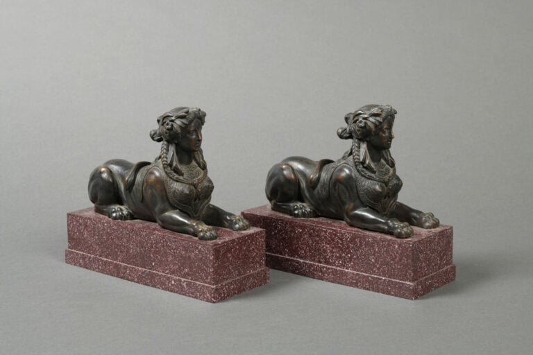 Paire de chenets en bronze à patine brune représentant des sphinges couchées su…