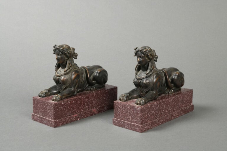 Paire de chenets en bronze à patine brune représentant des sphinges couchées su…