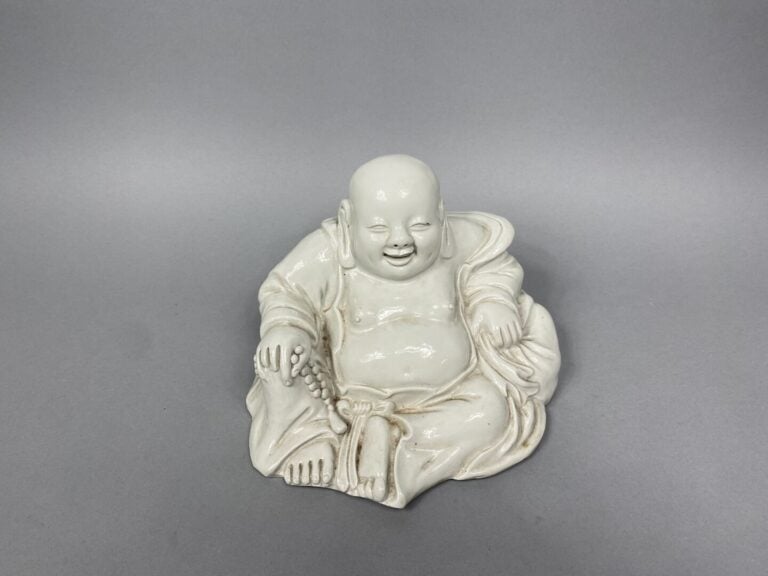 Chine - Bouddha rieur en céramique blanche représenté assis tenant un collier r…