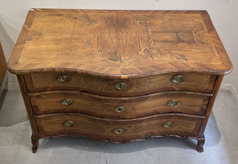 Commode en bois naturel à façade galbée ouvrant à trois tiroirs, ornementation…