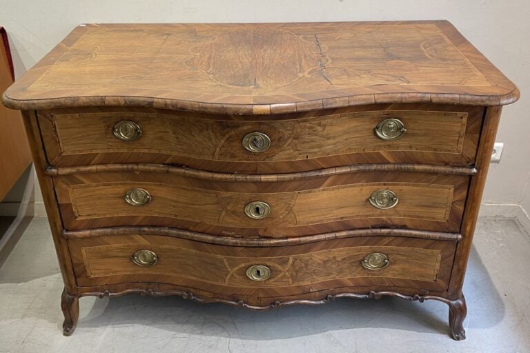 Commode en bois naturel à façade galbée ouvrant à trois tiroirs, ornementation…