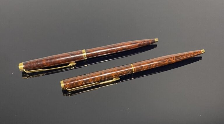 PARKER - Lot comprenant deux stylos à bille rétractable en métal doré et laque…