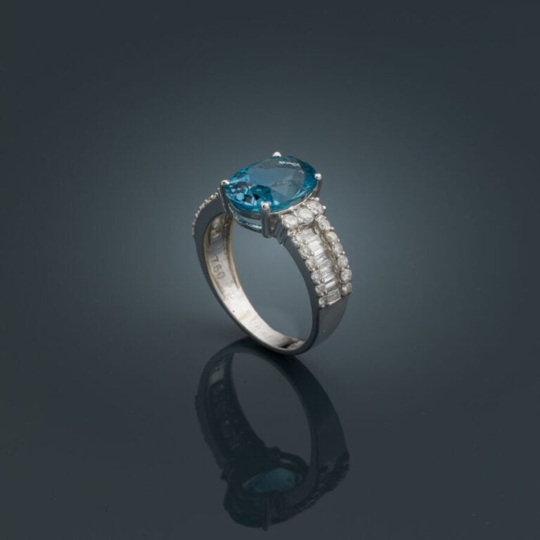BAGUE en or gris (750‰) serti d'une aigue-marine ovale (chocs), épaulée d'align…