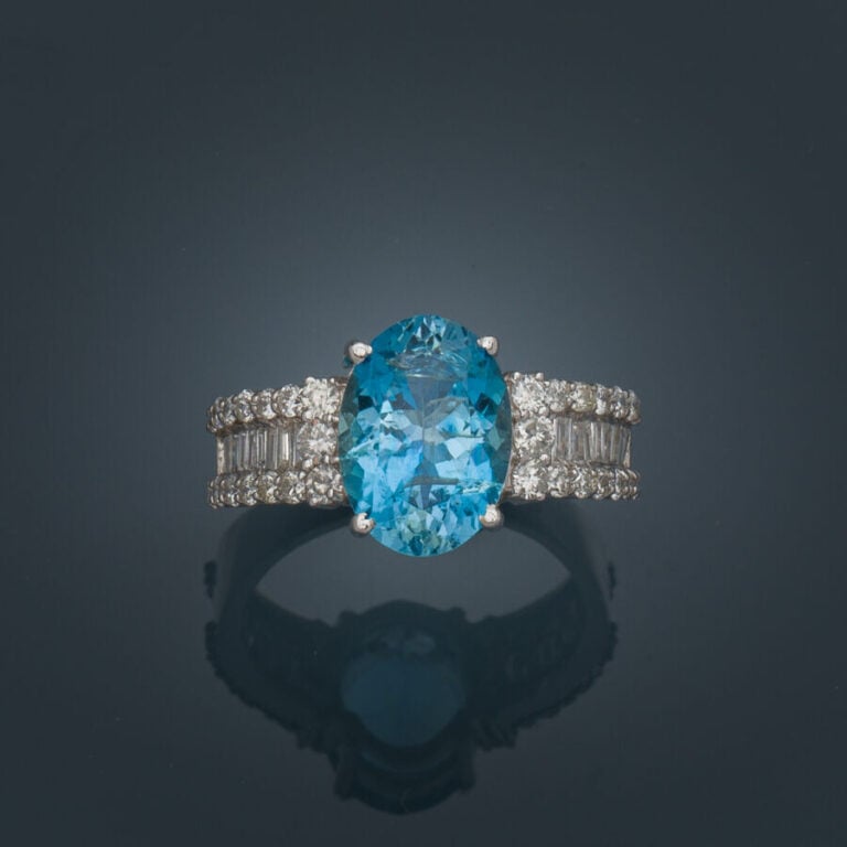 BAGUE en or gris (750‰) serti d'une aigue-marine ovale (chocs), épaulée d'align…