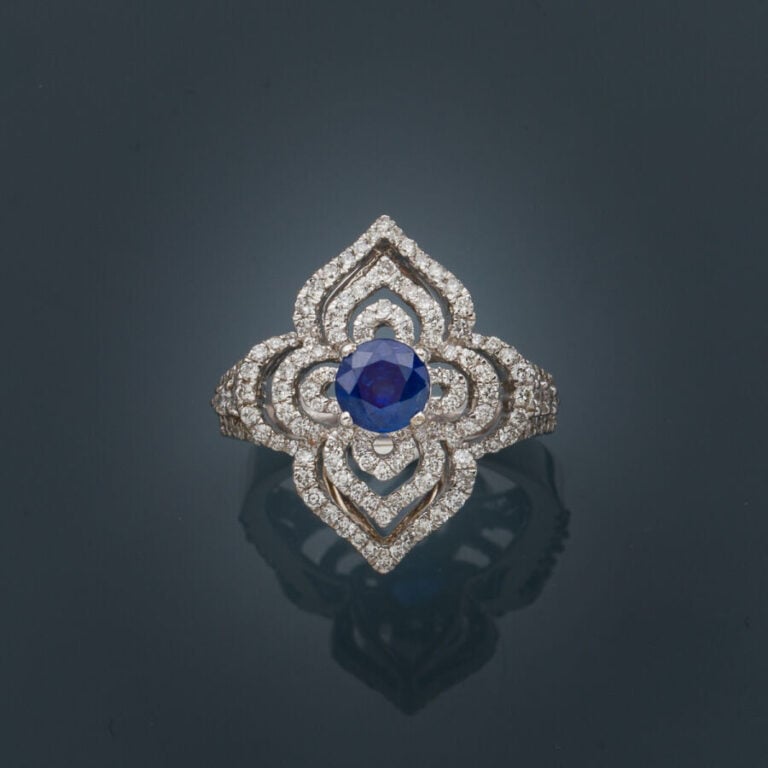 BAGUE "fleur stylisée" en or gris (750‰) ajouré, serti d'un saphir rond, entour…