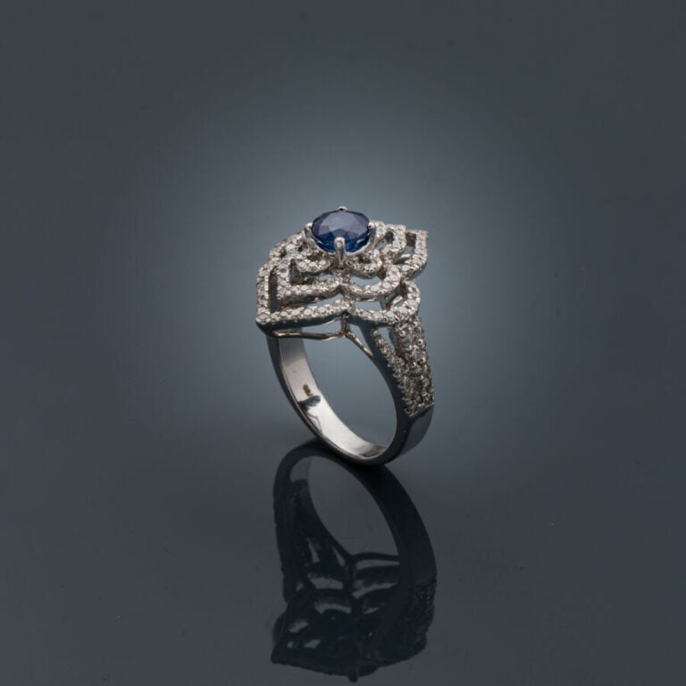 BAGUE "fleur stylisée" en or gris (750‰) ajouré, serti d'un saphir rond, entour…