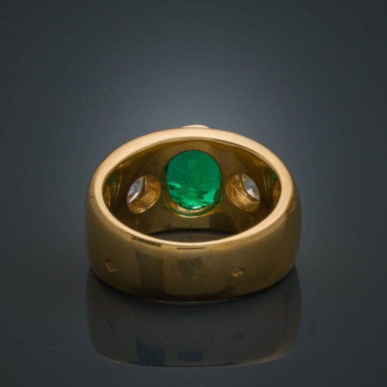 Large BAGUE en or jaune (750‰) serti d'une émeraude ovale (chocs), épaulée de d…