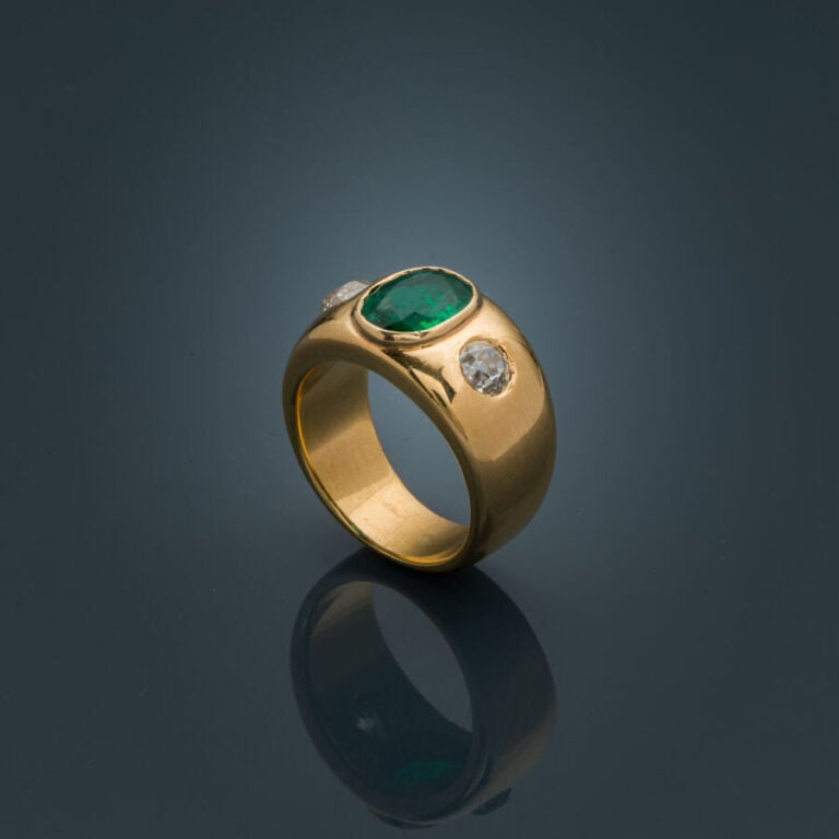 Large BAGUE en or jaune (750‰) serti d'une émeraude ovale (chocs), épaulée de d…