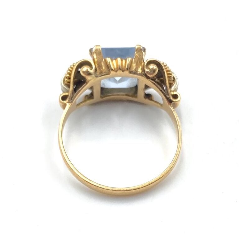 Bague en or jaune à deux boucles stylisées enserrant une pierre bleue rectangul…