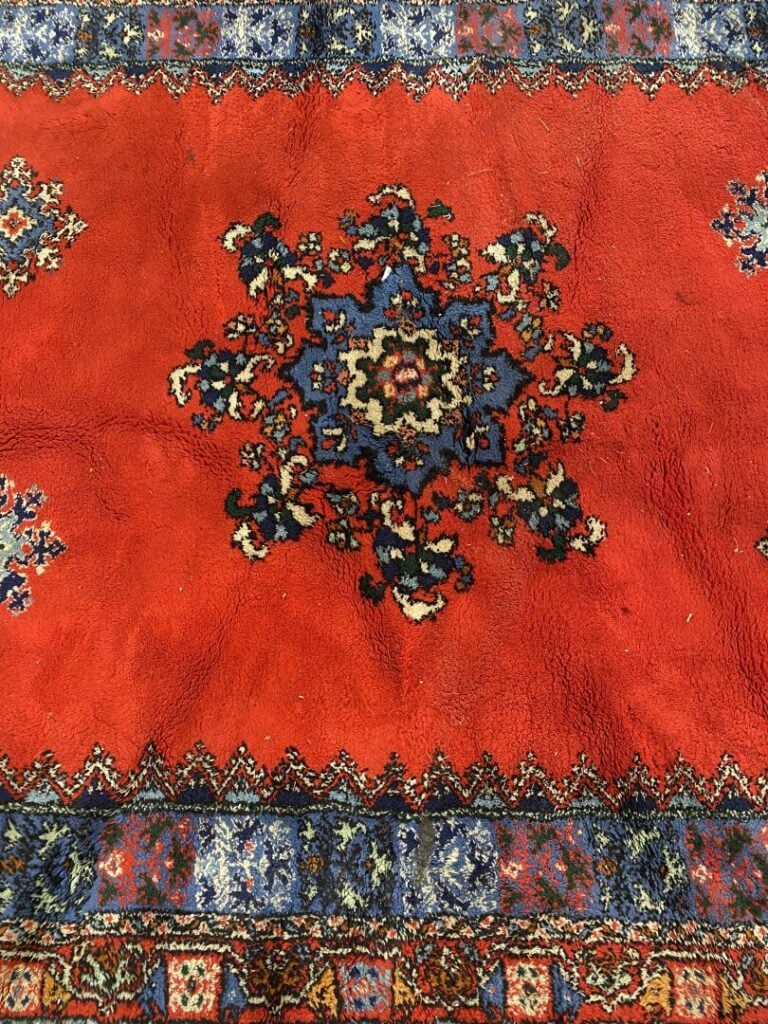 MAROC - Tapis en laine à fond rouge centré d'un motif floral, la bordure est so…