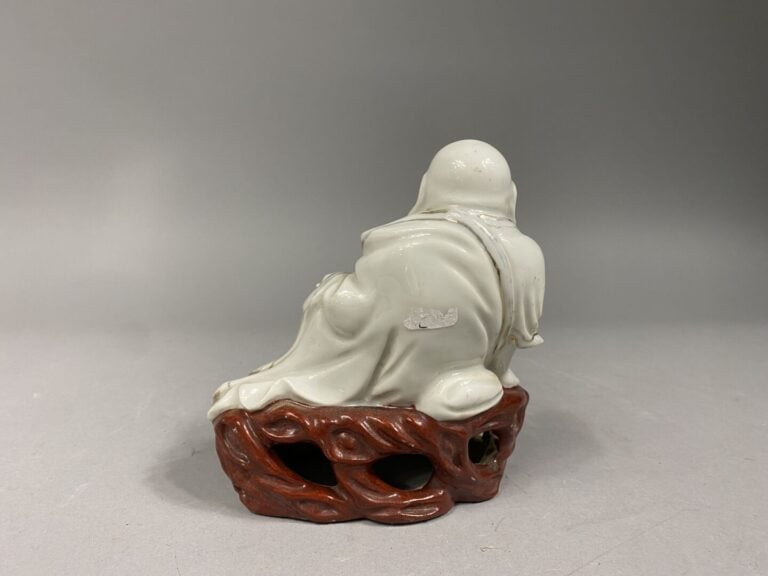 Petit bouddha en porcelaine émaillée représenté assis sur un rocher percé tenan…