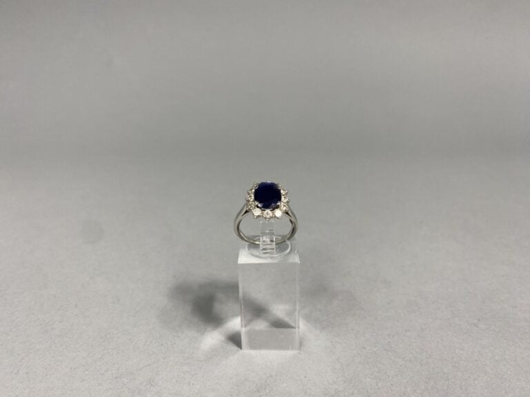 Bague marguerite en or gris (750) ornée d'un saphir foncé de taille ovale facet…