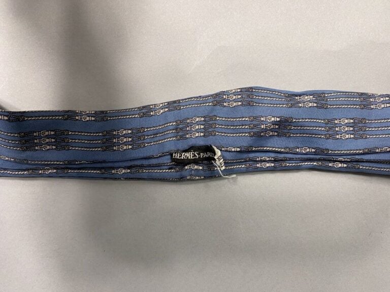 HERMÈS - Lavallière en soie bleue, à décor de sangles grises. - Bon état