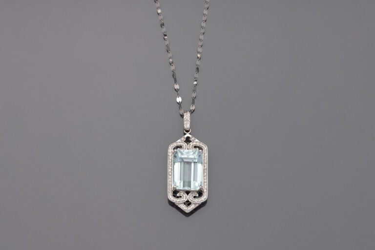 PENDENTIF et sa chaînette, en or gris (750‰) ajouré à motifs de volutes serti d…