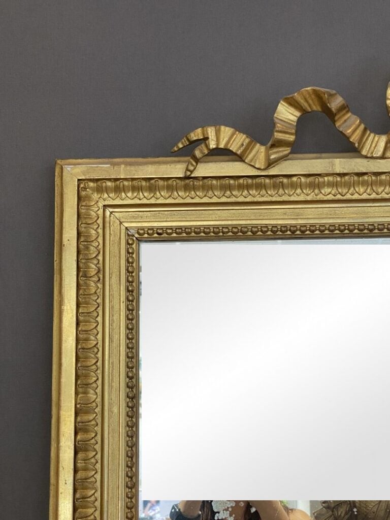 Grand miroir en bois mouluré, sculpté doré, à décor de frises de perles et feui…