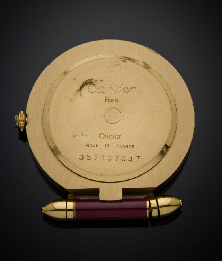 CARTIER - - MONTRE REVEIL DE CHEVET ronde en métal doré et laque bordeau. Cadra…