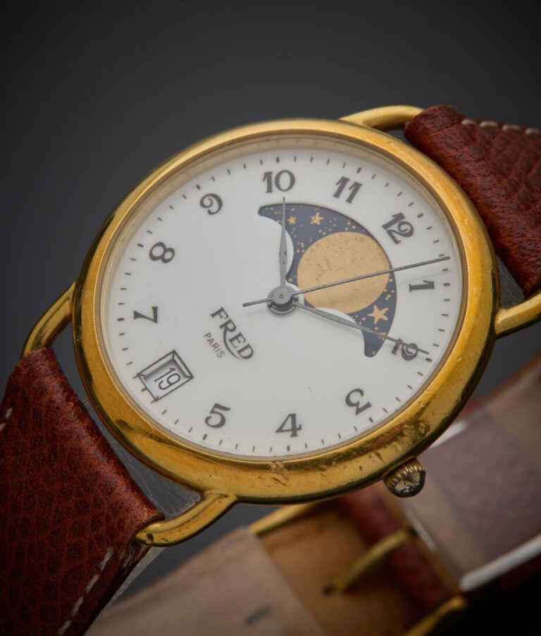 FRED - - BRACELET MONTRE ronde en acier et métal doré. Cadran émail blanc, phas…