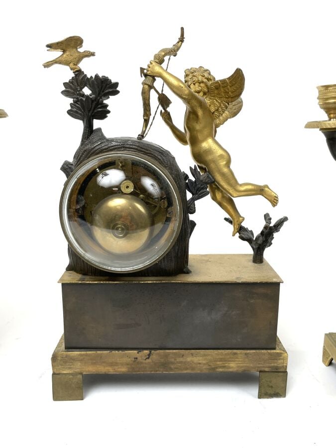 GARNITURE DE CHEMINEE comprenant une pendule à décor en relief d'un amour ailé…