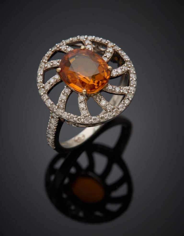 BAGUE "soleil" en or gris (750‰) ajouré, serti d'un saphir orange de forme oval…