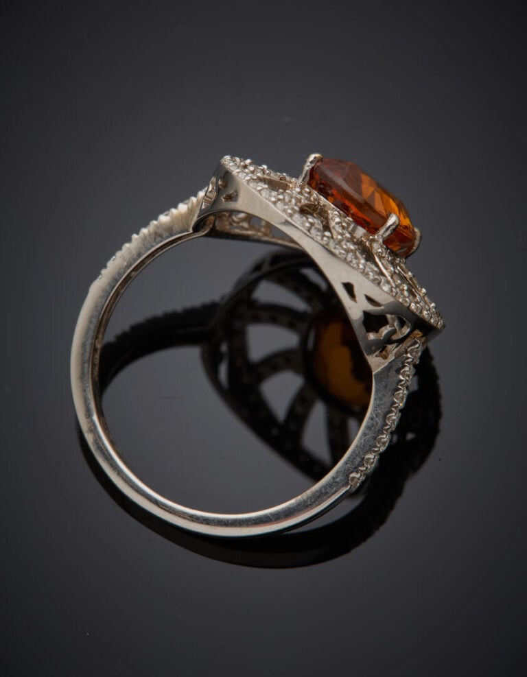 BAGUE "soleil" en or gris (750‰) ajouré, serti d'un saphir orange de forme oval…