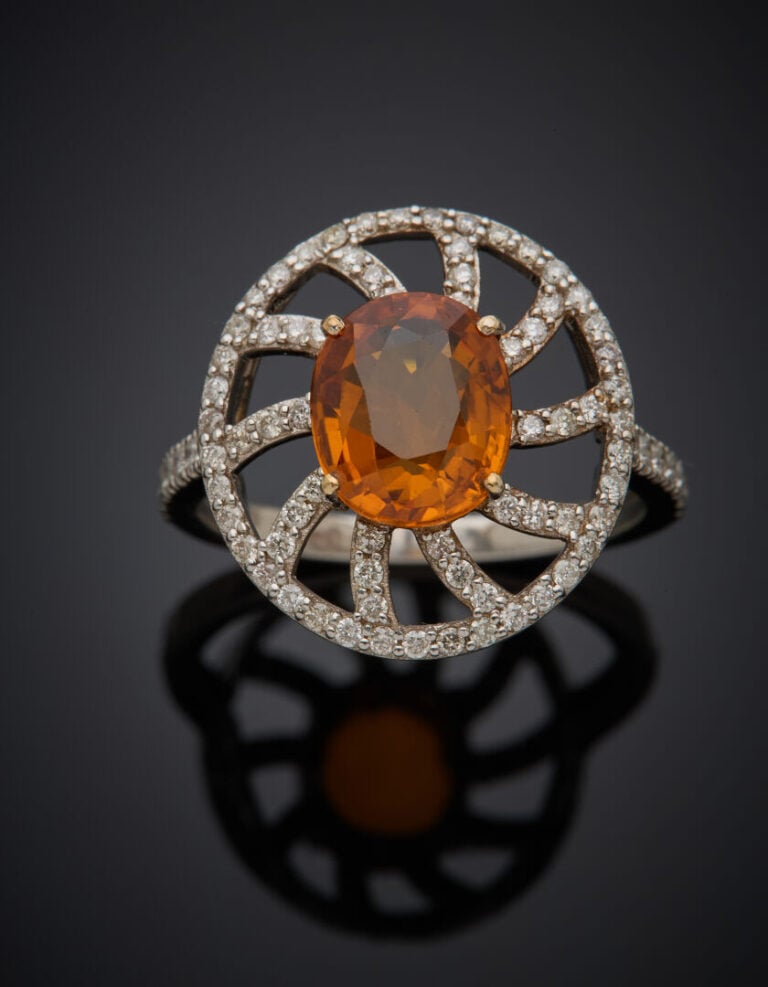 BAGUE "soleil" en or gris (750‰) ajouré, serti d'un saphir orange de forme oval…
