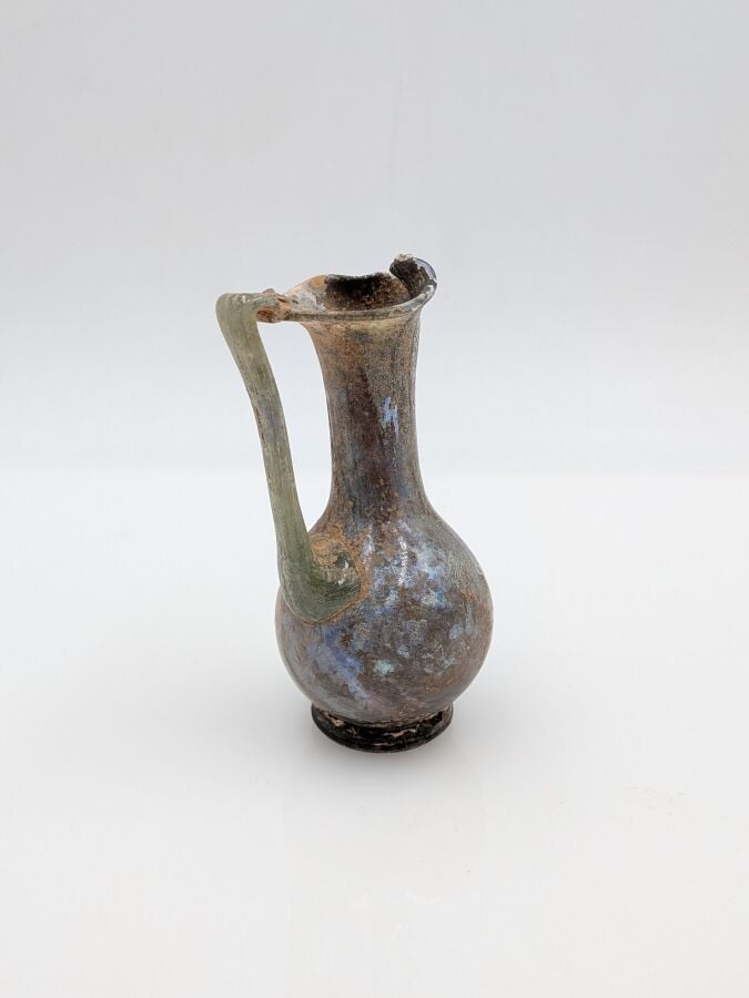 OEnochoé à lèvre pincée, à haut col et pied discoïde. Verre translucide violine…