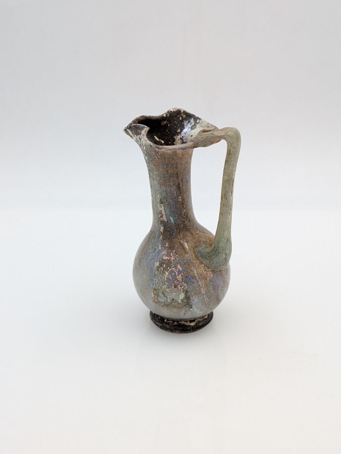 OEnochoé à lèvre pincée, à haut col et pied discoïde. Verre translucide violine…