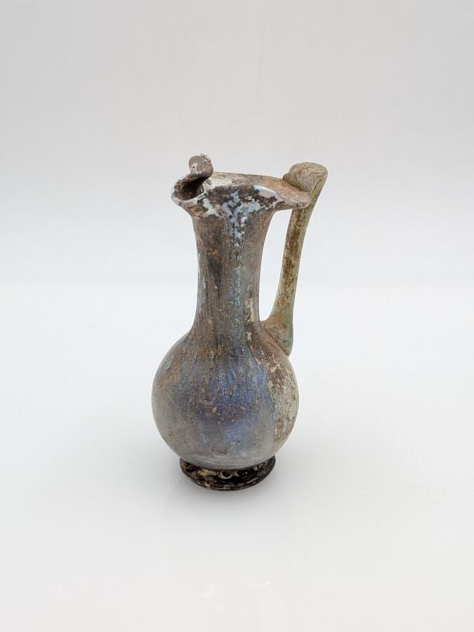 OEnochoé à lèvre pincée, à haut col et pied discoïde. Verre translucide violine…