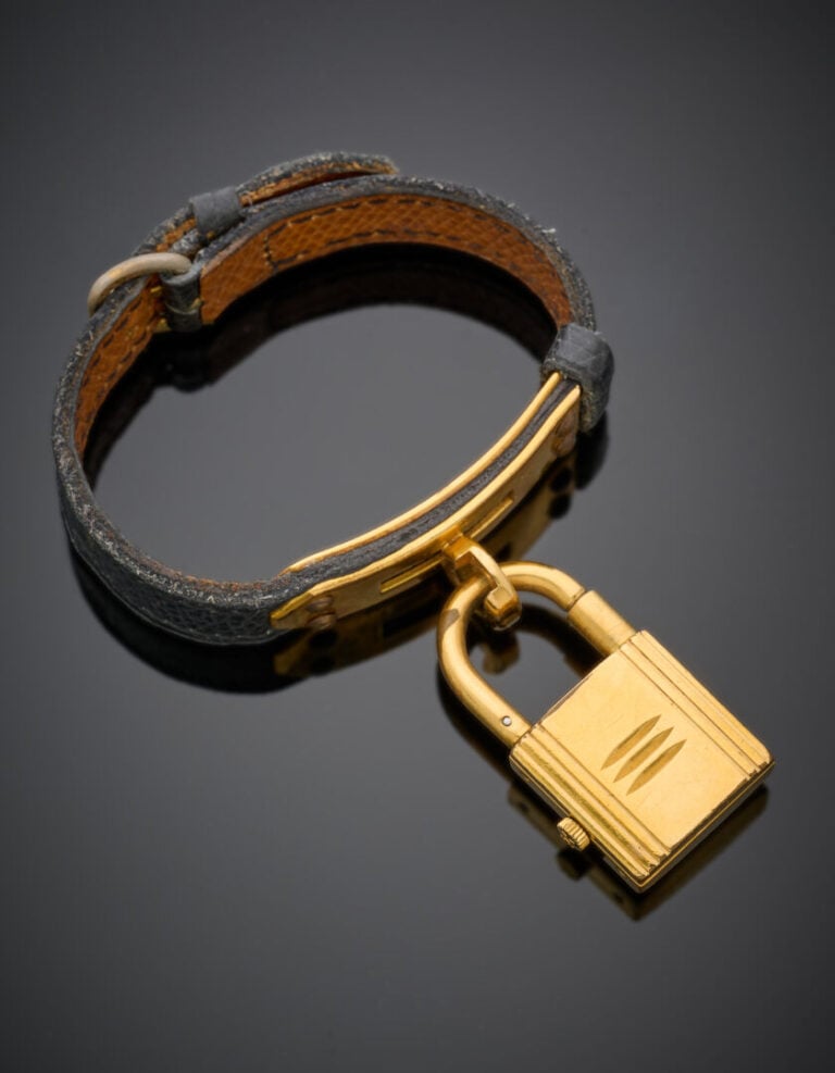 HERMES - BRACELET MONTRE "Kelly" en métal doré composé d'un bracelet en cuir. -…