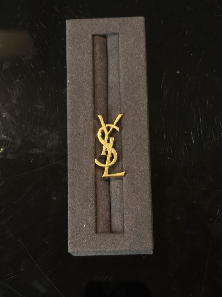YVES SAINT LAURENT - Pin's "YSL" en métal doré. - H : 3 cm