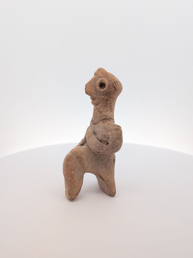Figurine assise stylisée, tenant un instrument indéterminé. - Terre cuite beige…
