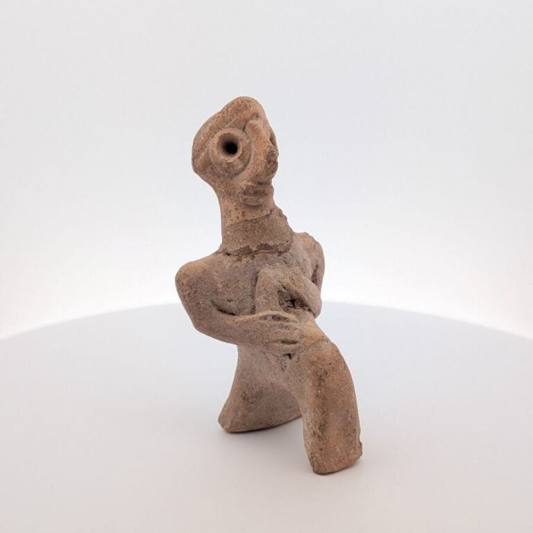 Figurine assise stylisée, tenant un instrument indéterminé. - Terre cuite beige…