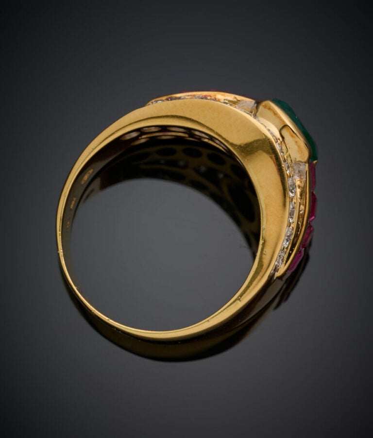 Large BAGUE en or jaune (750‰) serti d'une émeraude ovale, soulignée de rubis c…
