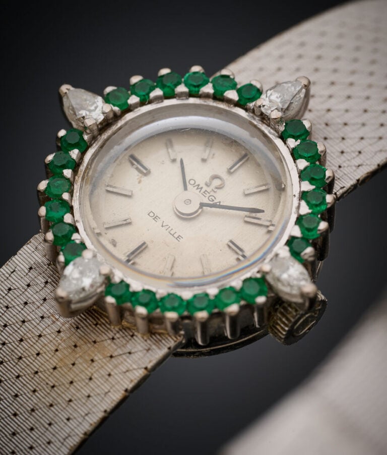 OMEGA - BRACELET MONTRE ronde de dame en or gris (750‰). Lunette sertie d'émera…